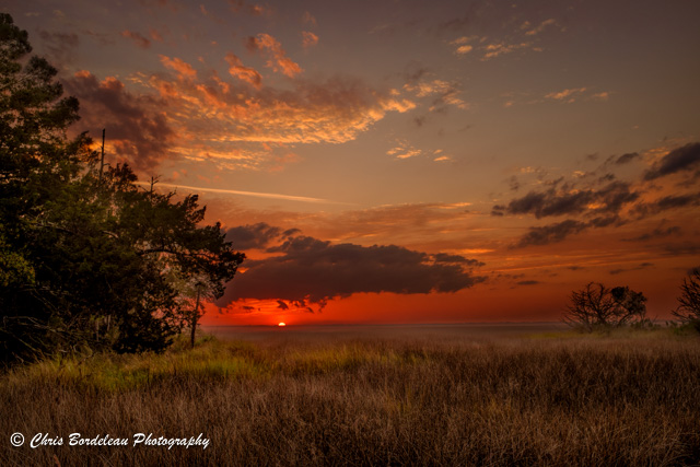 From the north end of Saint Simons Island after an evening storm the sun drops below the horizon over the salt marsh.